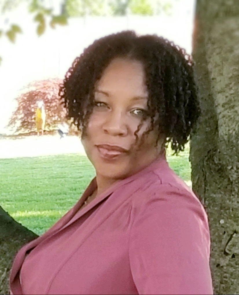Black woman wearing a pink suit jacket leaning against a tree
