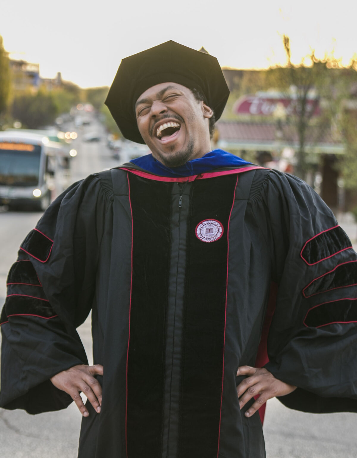 Black man smiling wearing PhD regalia.
