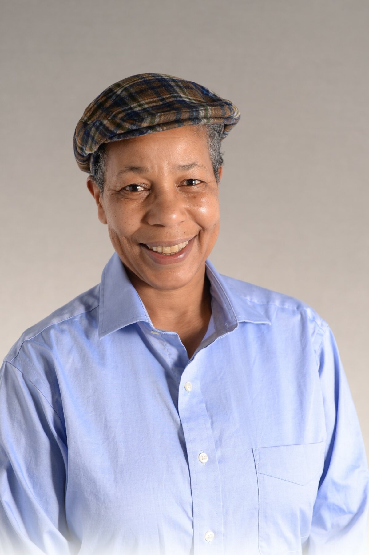 Black woman wearing a blue button-up shirt and a plaid cap.