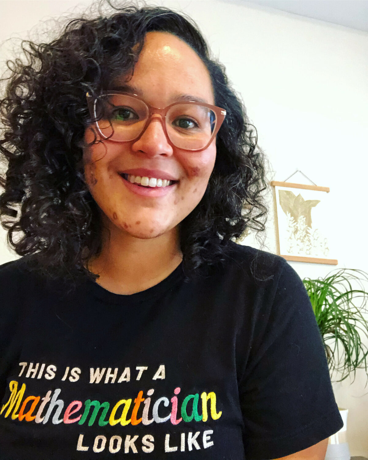 A Black woman wearing glasses and a black shirt with the words 